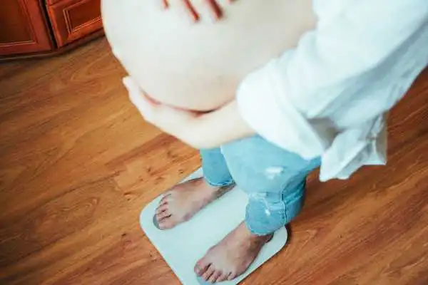 Image of woman weighing herself and experiencing weight gain through pregnancy Uppingham